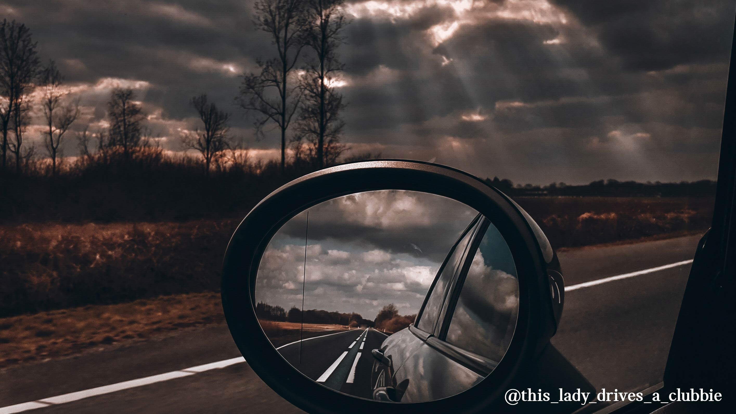  MINI Cooper mirror view on the road in an autumn landscape.